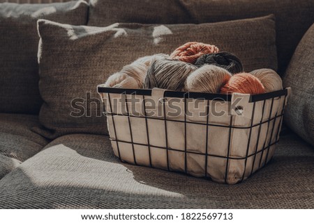 Basket of earth coloured skeins of yarn on a sofa, sunlight from the window on it, selective focus.