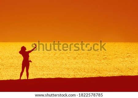 Silhouette of a woman taking a selfie photo on the seashore during sunset. . High quality photo