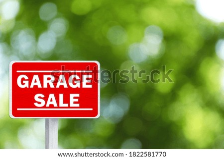 Sign with phrase GARAGE SALE on blurred green background, bokeh effect