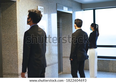 Office workers wearing a mask and keep distancing while waiting the elevator. for prevent infection and reduce spread of Covid-19 virus