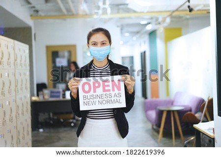 office Reopening business adapt to new normal in the novel Coronavirus COVID-19 pandemic. business woman wearing medical mask holding open sign “OPEN BUSINESS AS NEW NORMAL” on front door