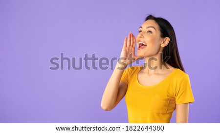 Attention, People. Portrait of happy female model holding hand near mouth, screaming aside at copy space isolated over purple studio background. Lady making offer yelling to free space, banner,