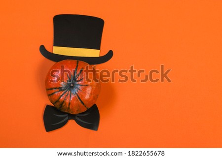 Happy Halloween pumpkin on orange background, paper hat, bow tie, flat lay. Atmospheric image. Autumn postcard. Copy space
