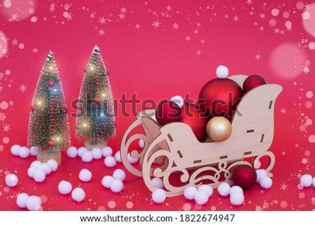 wooden sleigh with Christmas balls and Christmas trees on a red background