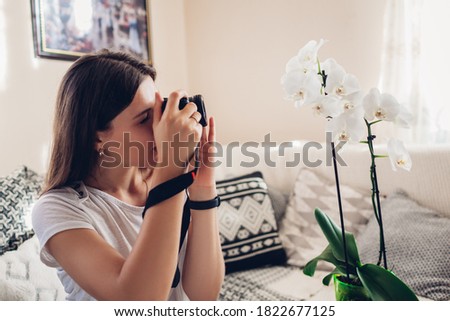 Woman photographer takes picture of blooming orchid using camera. Freelancer works from home during covid