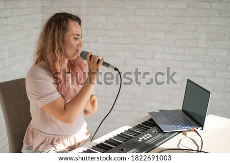 A woman sings into a microphone and shoots a video blog on a laptop