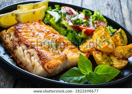 Fish dish - fried cod fillet with potatoes and vegetable salad on wooden table 