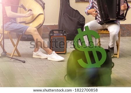 two street musicians, one on a bandura and the other on an accordion. in front of them is a bag with a big green dollar sign. sun light in right corner of photo