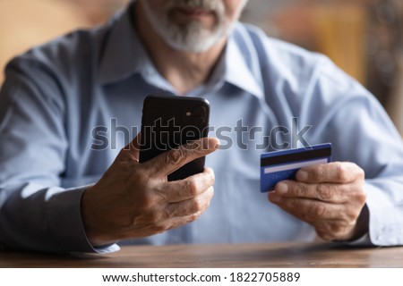 Close up of modern mature man hold cellphone and credit card make online payment or purchase form home. Smart senior male pay bills or shop on internet using smartphone. Elderly technology concept Royalty-Free Stock Photo #1822705889