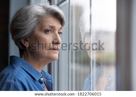 Unhappy elderly Caucasian 60s woman look in window distance mourning or yearning at home. Sad mature grey-haired female lost in thoughts feel lonely abandoned in retirement house. Solitude concept. Royalty-Free Stock Photo #1822706015
