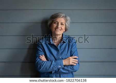 Profile picture of smiling elderly 60s grey-haired woman stand isolated on grey wooden wall background at home. Portrait of happy mature female feel optimistic overjoyed, have pleasant retirement.