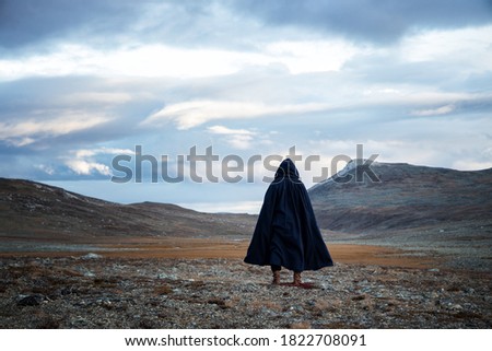 Back view silhouette of traveler man standing on the mountain.  A mysterious cloaked man. Medieval man in hooded cloak. Royalty-Free Stock Photo #1822708091