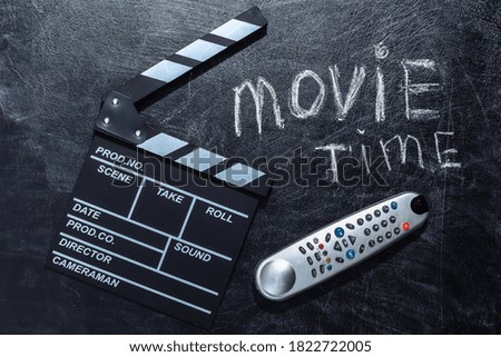 Movie time. Movie clapper board and tv remote on chalk blackboard.