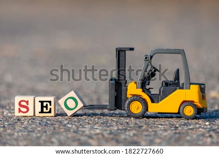 A toy forklift lifts a block with the  letter O to complete the word SEO (search engine optimization abbreviation) from the asphalt.