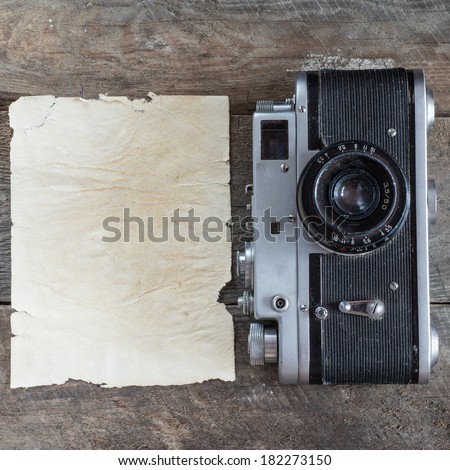 Vintage photo camera on a wooden table with paper sheet