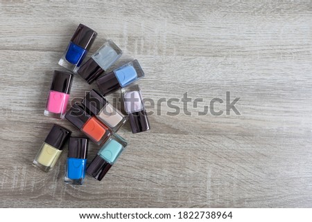 Collection of multi-colored bottles of nail polish. Layout for design on a gray background and a wooden table.