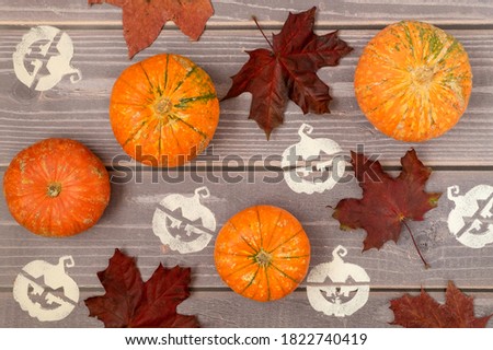 Halloween background of ripe small pumpkins, fallen red maple leaves and stenciled Halloween symbols on a wooden surface. Horizontal orientation, selective focus, top view.
