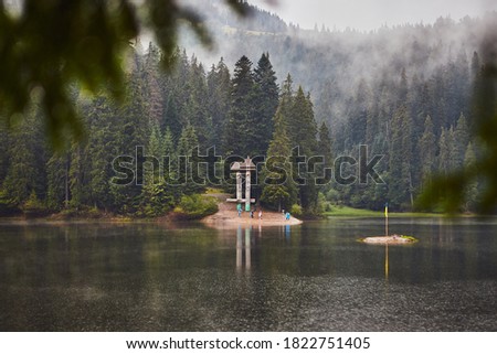 Mountain Lake Synevir in the rainy foggy summer day in Carpathian, Ukraine.  Beautiful nature scenery outdoors. Coniferous forest with tall trees on the shore