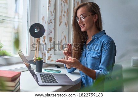 Happy young smiling casual woman learning and communicates in sign language online at a laptop at cozy comfy home by the window 