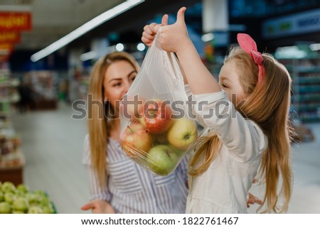 Happy little girl picked up a full package of fresh juicy apples in the supermarket.