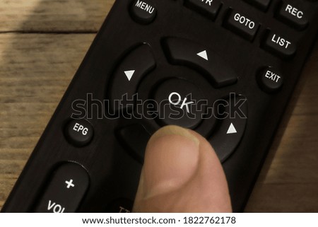 The thumb presses the OK button on the remote control. It can be used as a symbol of readiness for action, a change of scenery. Selective soft focus.
