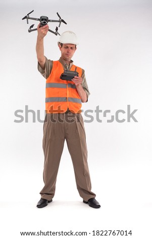 Surveyor with a quadcopter. Man in orange vest is holding a quadcopter. Concept - geodesic studies using a quadcopter. Surveyor launches a drone. Light background. Modern surveyor equipment.