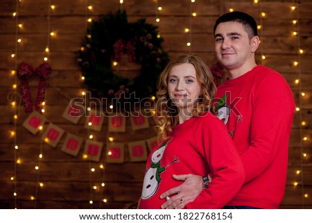 Close up of happy married couple bonding next to Christmas tree. Best Christmas gift. Young pregnant woman with her husband decorate the Christmas tree. A young loving couple in cozy sweaters.