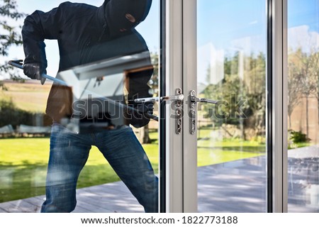 Burglar or thief breaking into a home through window with a crowbar Royalty-Free Stock Photo #1822773188