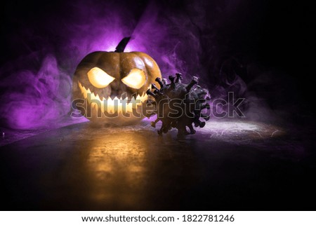 Halloween during Corona virus global pandemic concept. Glowing pumpkins and Covid novel on dark with thematic spooky decorations. Halloween pumpkin on foggy backlight. Selective focus