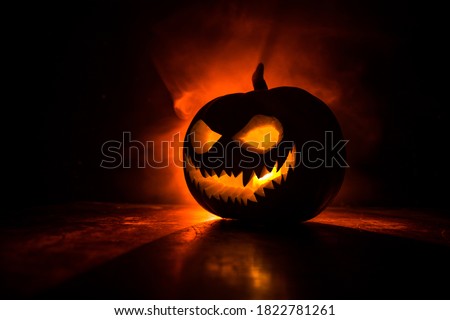 Halloween pumpkin smile and scary eyes for party night. Close up view of scary Halloween pumpkin with eyes glowing inside at black background. Selective focus Royalty-Free Stock Photo #1822781261