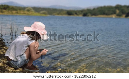 
girl taking a picture of fish in a swamp with a pink hat