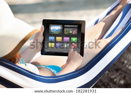 Woman using digital tablet while relaxing in hammock at beach