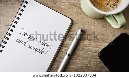 Keep it short and simple!. Flat lay. Work area with notepad, pen, cell phone and a cup of coffee.  Royalty-Free Stock Photo #1822837334
