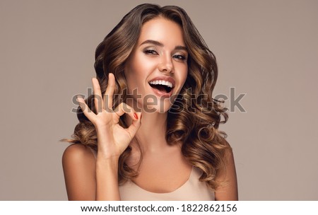 Happy  girl with curly hair   smiling and showing OK sign . Presenting your product. Expressive facial expressions