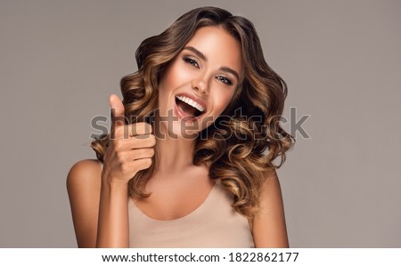 Beautiful  happy  woman with curly hair   smiling and showing thumb up positive  sign . Presenting your product. Expressive facial expressions
