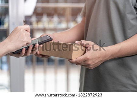 Delivery man and women appending signature in digital mobile phone after receiving parcel from courier at home 