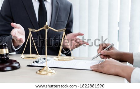 A male lawyer or a judge counseling clients about judicial justice and prosecution with scales, judges gavel, legal documents legal services concept.