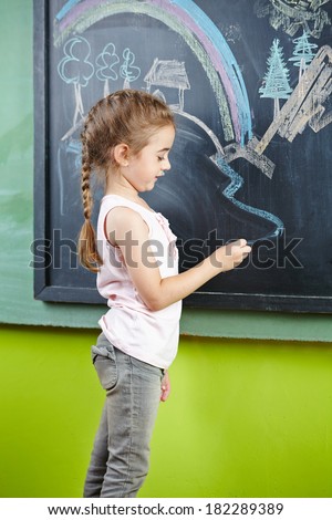 Girl drawing a picture on a bloackboard with chalk in the kindergarten