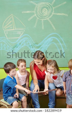 Children in preschool reading book together with a nursery teacher