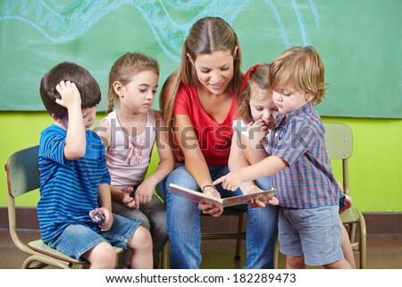 Children and nursery teacher reading book together in kindergarten