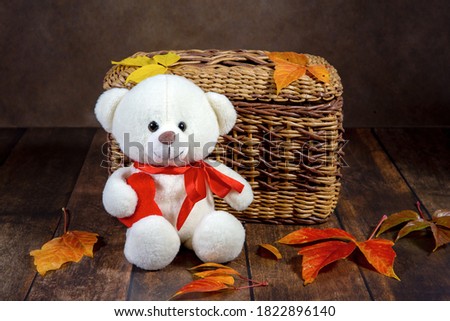 Wicker box with a children's toy bear on a dark background with autumn leaves