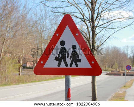 A triangle road sign telling drivers to be cautious of school children in the area. The sign depicts a triangle with a red border and two stick figure children inside of it.