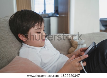Child boy sitting on sofa watching cartoons on mobile phone, School kid using cellphones learning lesson on internet,Home schooling, Distance learning online education concept