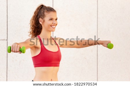 Optimistic motivated young female in activewear doing exercise with small dumbbells while training muscles during fitness workout Royalty-Free Stock Photo #1822970534