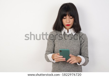 Portrait of excited Young businesswoman with retro short hairdo wearing casual clothes standing over isolated white background winking and eye hold smart phone use read social network news 