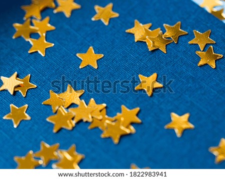 Gold star glitter confetti splashed on blue paper background. Festive twinkle glitter background.