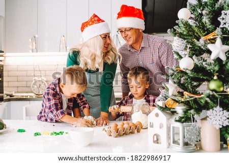 Family of two twins boys and age parents preparing cookies for Christmas ot New Year in light kitchen wearing Santa hats