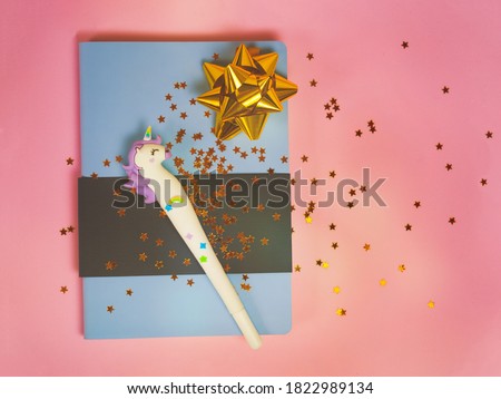 Blue notebook with with cute unicorn pen and gold bow and stars glitter on pink background. Girls note, magic diary with unicorn.