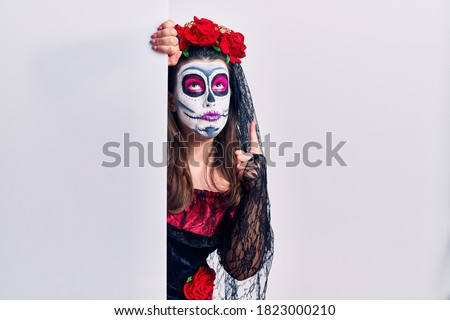 Young woman wearing day of the dead custome holding blank empty banner pointing up looking sad and upset, indicating direction with fingers, unhappy and depressed. 