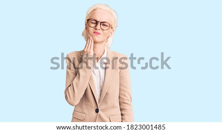 Young blonde woman wearing business clothes and glasses touching mouth with hand with painful expression because of toothache or dental illness on teeth. dentist 